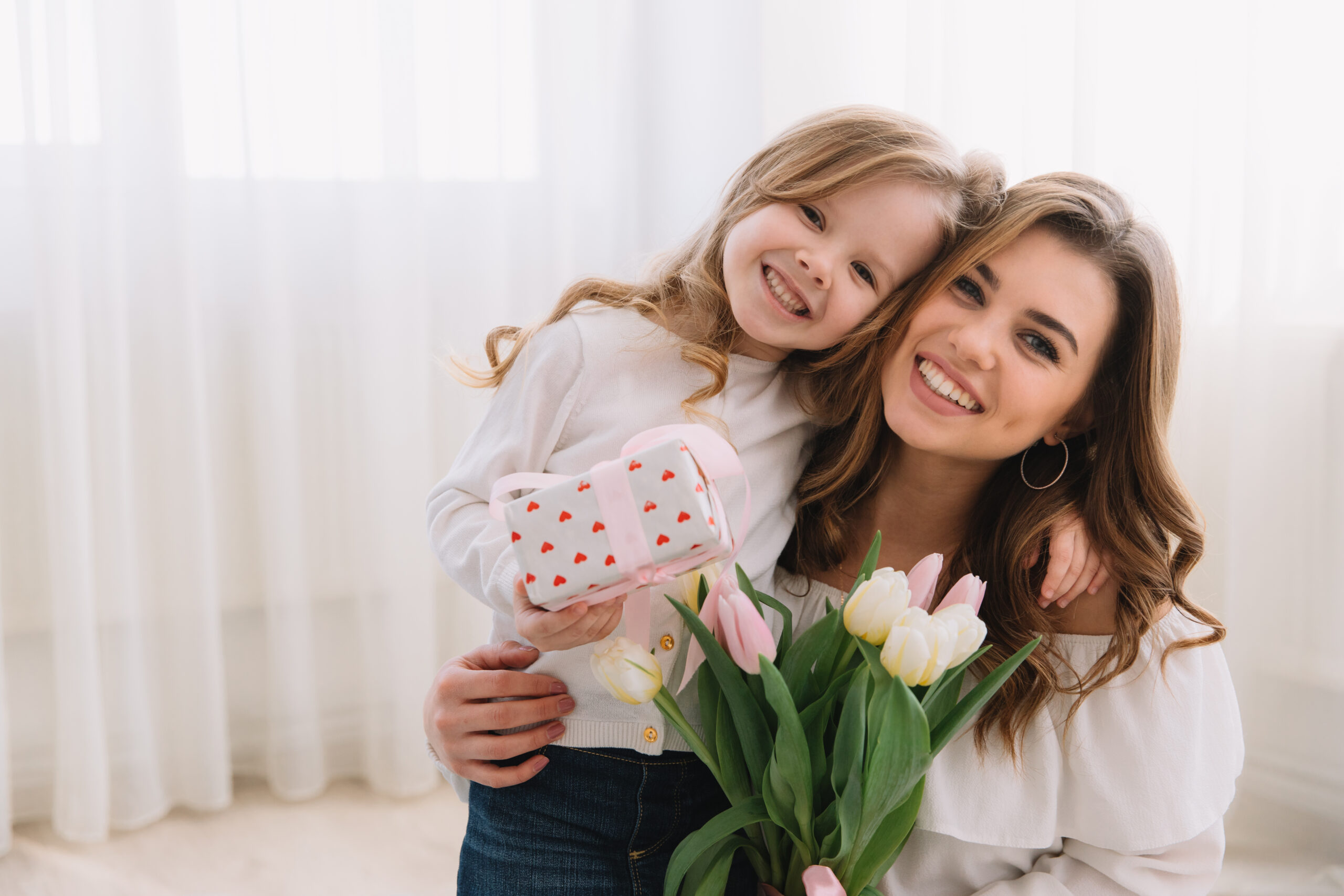 Happy mother's day. Child daughter congratulates moms and gives her flowers tulips and gift.