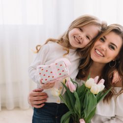 Happy mother's day. Child daughter congratulates moms and gives her flowers tulips and gift.
