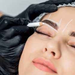 Markup with pencil on eyebrows of young woman while permanent make up.